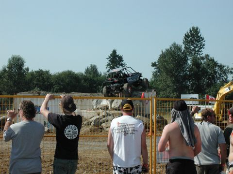 Custom buggy with number 83 airborne over rocks, spectators behind fence.