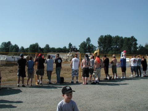 Spectators watching an off-road event behind a fence with construction in the background.