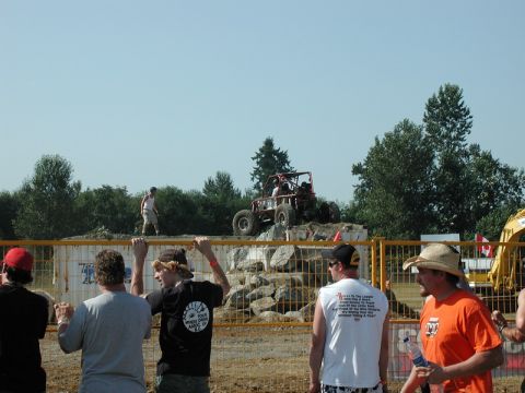 Red off-road buggy on a rocky obstacle course with spectators.