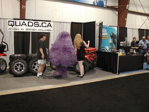 Red ATV at an event booth with a purple mascot costume and tires on display.