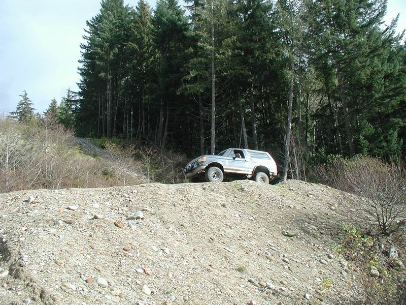 Silver Ford Bronco on a gravel hill with a forest backdrop.