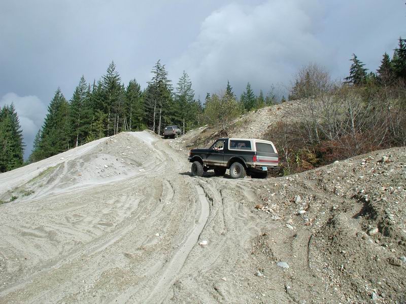 Ford Bronco driving up a sandy hill on a dirt road.