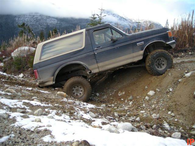1980s Ford Bronco climbing a steep, muddy, and snowy off-road trail.