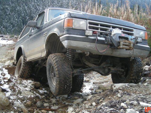 Lifted 1980s Ford Bronco on a rocky, muddy trail with a winch.