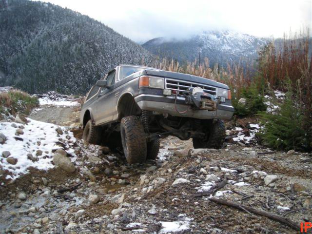 Lifted 1985 Ford Bronco with winch on rocky, snowy mountain trail.