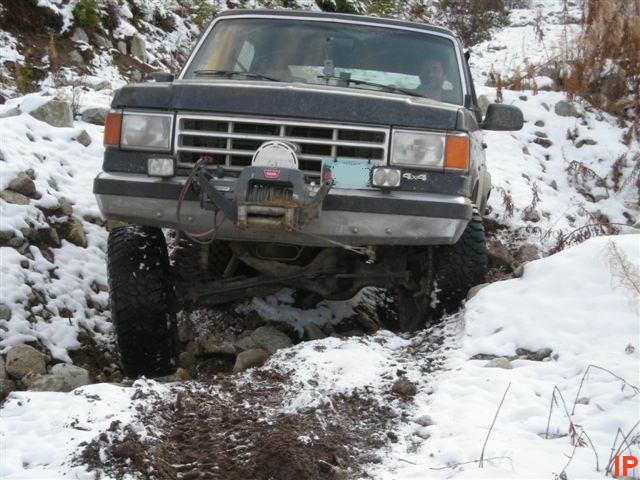 1985 Ford Bronco navigating a snowy, rocky trail with a front winch.