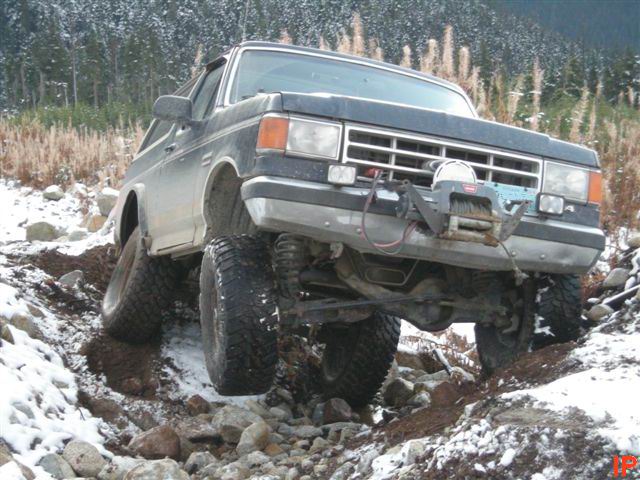 1985 Ford Bronco driving through snow and rocks, front view with winch.