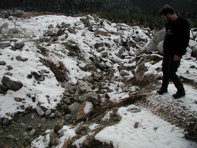 A man walks through a rocky, snow-covered landscape.