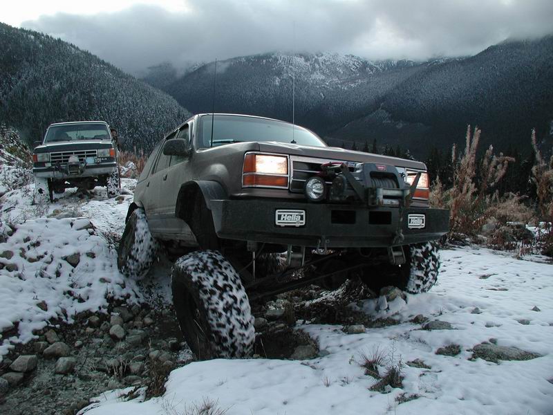 Two modified SUVs off-roading on a snowy mountain trail.