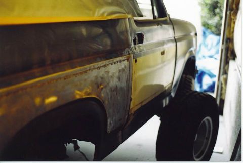 1985 Ford Bronco - Close-up side view of a yellow Ford Bronco undergoing restoration, showing exposed metal and rust on the lower body panels and door. The ve…