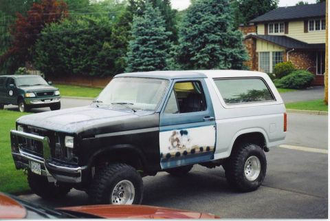 1985 Ford Bronco - A two-tone blue and white Ford Bronco is parked on a residential street. The front of the vehicle is dark blue and appears to be undergoing…