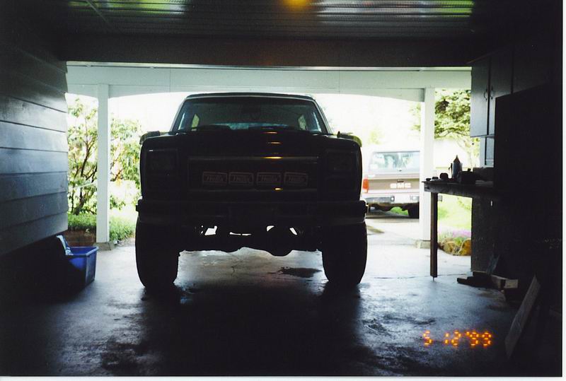 Front view of a dark, lifted pickup truck in a garage with another truck in the background.