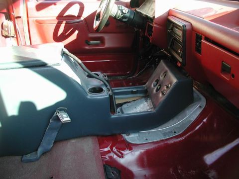 1990 Ford F-250 - The interior of a red Ford F-250 pickup truck shows a custom dark blue center console with cup holders and a storage compartment. The dashb…