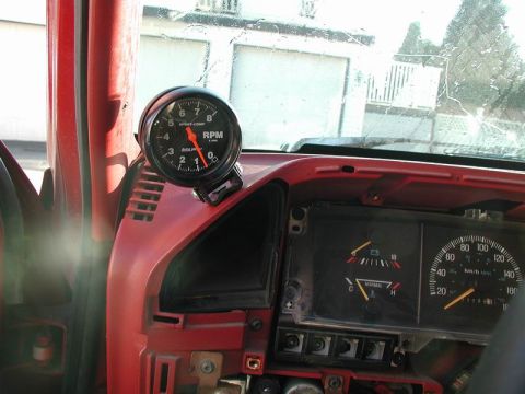 1990 Ford F-250 - The interior of a red Ford F-250 shows a mounted tachometer above the dashboard, with the speedometer and other gauges visible to the right.