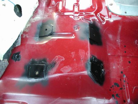 1990 Ford F-250 - The red painted interior floor of a vehicle shows several black metal patches welded in place over rust or damage. Some patches have visibl…