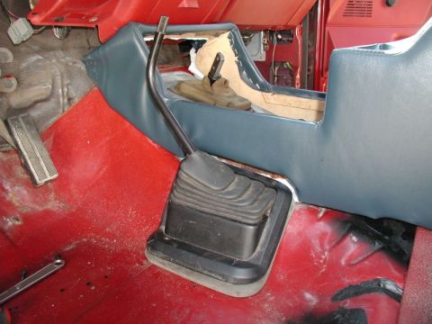 1990 Ford F-250 - The interior of a vehicle shows a manual transmission shifter and a blue vinyl center console. The red floor is visible with a metal brake…