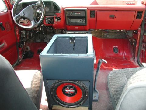 1990 Ford F-250 - The interior of a red Ford F-250 pickup truck, featuring a custom center console with a subwoofer. The dashboard and steering wheel are vis…