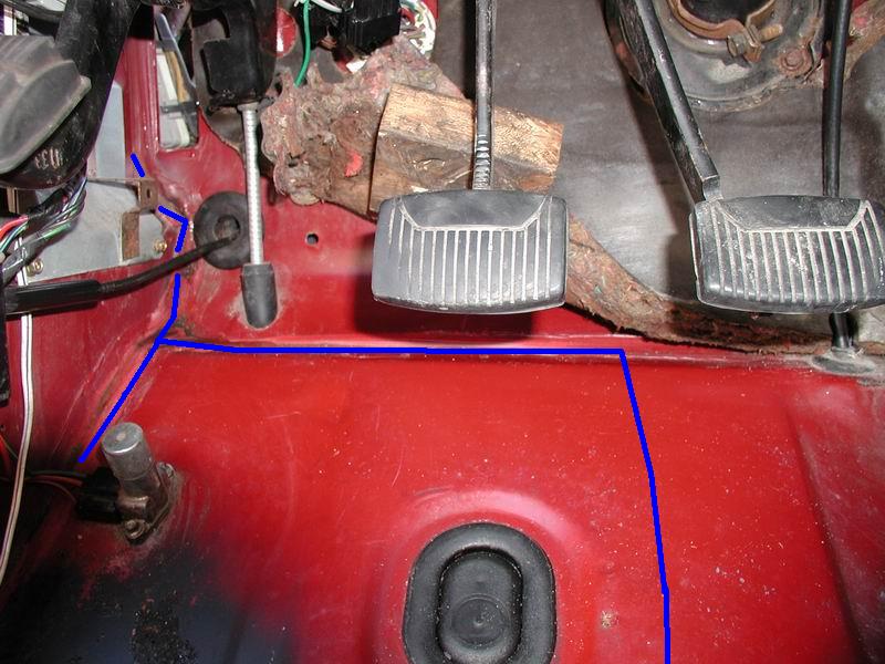 Interior of a red vehicle showing pedals and wiring with blue lines on the floor.