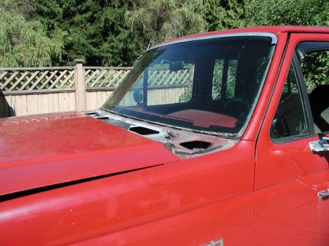 1990 Ford F-250 - Close-up of the front passenger side of a red Ford pickup truck, showing the hood, windshield frame, and part of the door. The windshield a…