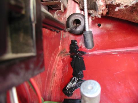 1990 Ford F-250 - A close-up view of a red vehicle's interior shows black sealant applied over wiring. A black rubber grommet and a metal rod with a black ca…