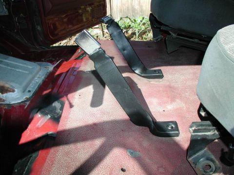1990 Ford F-250 - The interior of a vehicle shows two black seatbelt assemblies mounted to the floor. The floor is red with some rust and wear visible.