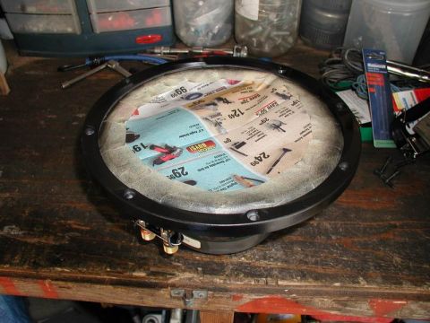 1990 Ford F-250 - A disassembled speaker with a circular opening covered in newspaper ads is shown on a wooden workbench. The speaker has a black metal frame…