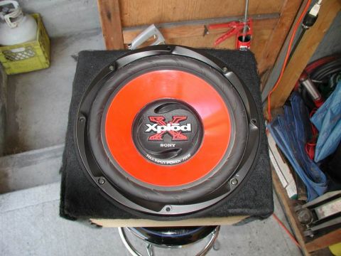 1990 Ford F-250 - A close-up view of a Sony Xplod subwoofer in a black carpeted enclosure. The subwoofer cone is bright orange with a black spider and a silv…
