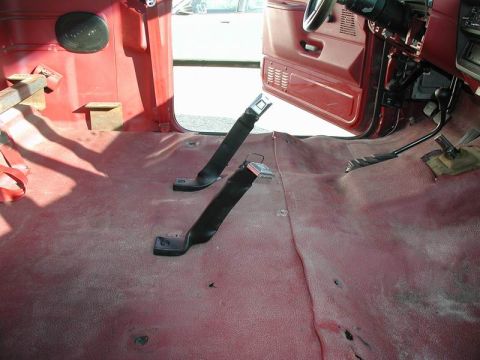 1990 Ford F-250 - The interior of a red Ford F-250 pickup truck is shown, with the driver's side door open. The floor is covered in red carpet and features t…