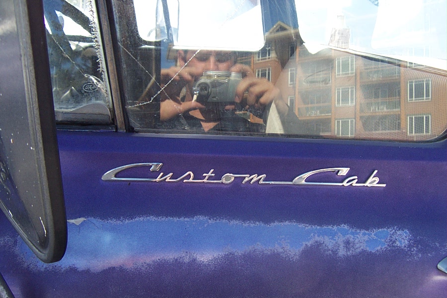 Close-up of a purple truck door with a 'Custom Cab' emblem. Reflection in window shows a person taking the photo