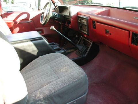 1990 Ford F-250 - The interior of a red Ford F-250 pickup truck shows a bench seat with a patterned fabric insert, a center console with cup holders, and a m…