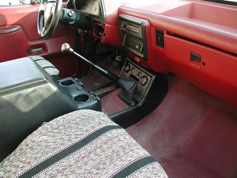 1990 Ford F-250 - The interior of a pickup truck features a red dashboard and floor mats, a black center console with cup holders, and a manual transmission…
