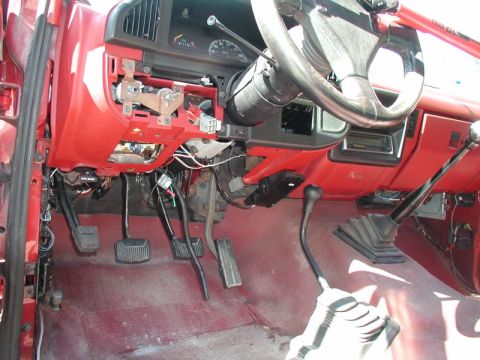1990 Ford F-250 - The interior of a red Ford F-250 truck shows the dashboard, steering wheel, and manual transmission shifters. The dashboard is partially di…