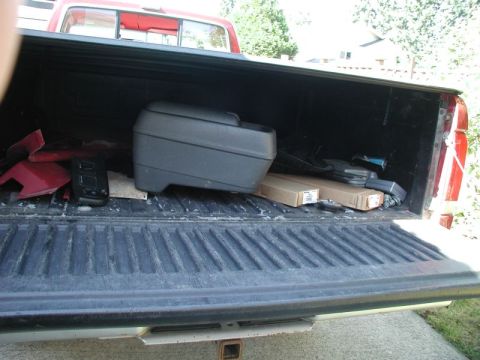 1990 Ford F-250 - The open tailgate of a red and white Ford pickup truck bed is filled with various items, including a black storage box, red plastic parts,…