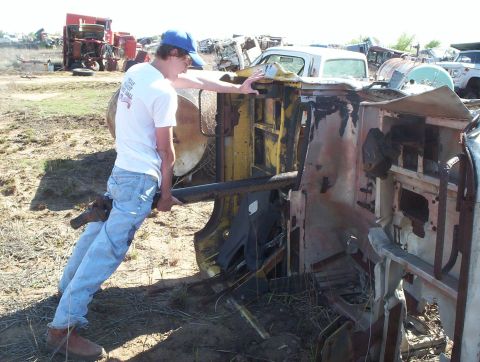 1990 Ford Bronco - A person interacts with an overturned vehicle chassis in a junkyard setting with multiple other vehicles present.