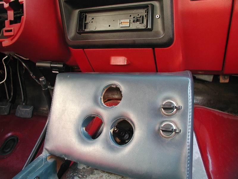 Interior view of a vehicle dashboard with a stereo and a blue padded panel with cutouts.
