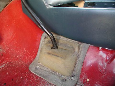 1990 Ford F-250 - A close-up view of the interior floor of a vehicle, showing a black gear shift lever emerging from a worn, tan boot on a red floor.