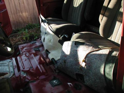 1990 Ford F-250 - The interior of a vehicle shows the floor with exposed metal and some insulation removed. The front seats are visible, with one seat partia…