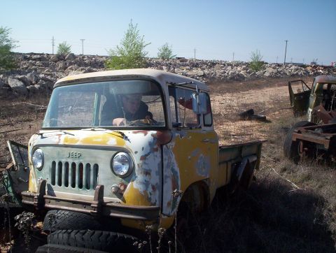 1990 Ford Bronco - This weathered Jeep FC-150 pickup truck sits in a junkyard, showing signs of age and disuse.