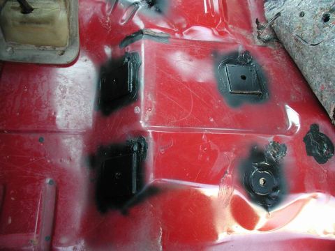 1990 Ford F-250 - The red painted interior floor of a vehicle shows several black square patches applied over areas that have been treated with a rust inhibi…