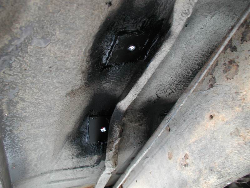 Underneath view of vehicle frame with two black square plates attached.