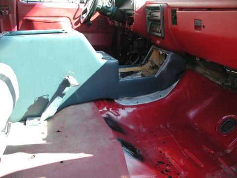 1990 Ford F-250 - The interior of a vintage Ford F-250 pickup truck shows a red dashboard and door panels, a blue center console with a seatbelt, and a red f…