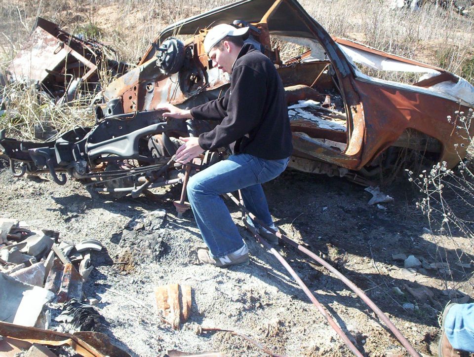 Burnt out vehicle side view with a person examining the engine compartment