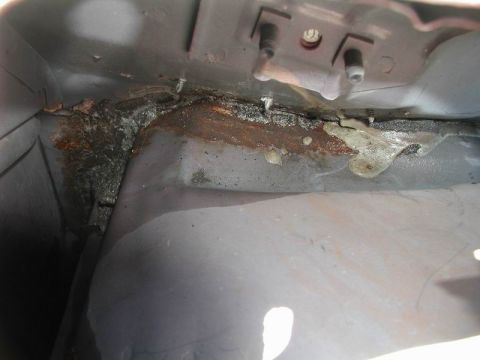 1990 Ford F-250 - Close-up view of the underside of a vehicle, showing significant rust and a thick, yellowish substance along a seam. The metal appears to b…