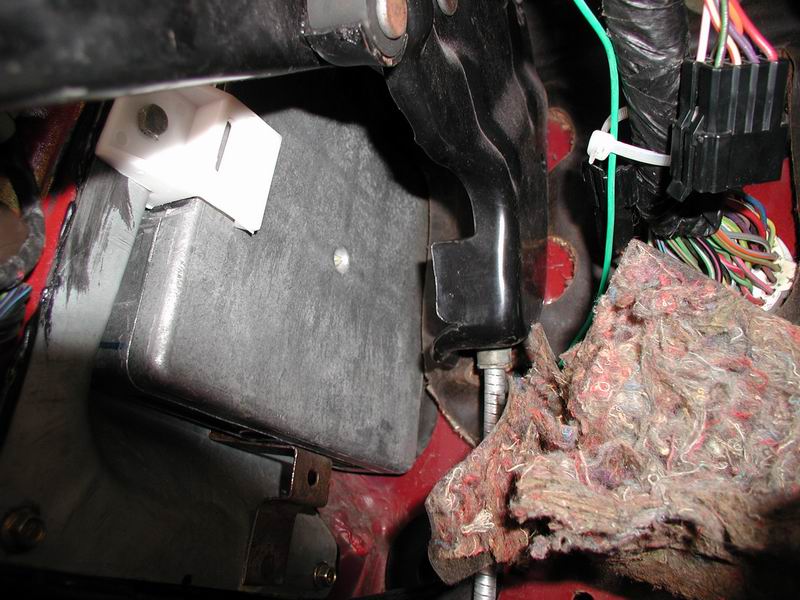 Close-up of vehicle interior footwell showing wiring, bracket, and a gray box.