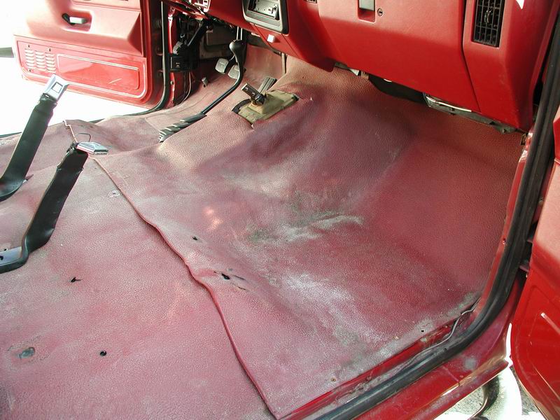 Interior of a red 1990 Ford F-250 showing the driver's side floor and lower dashboard.