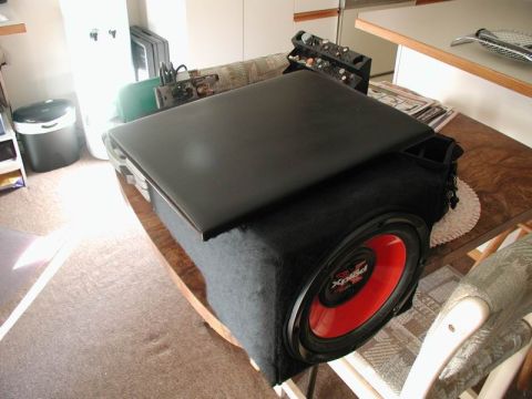 1990 Ford F-250 - A black subwoofer is placed on a wooden table, with a black laptop resting on top of it. The subwoofer has a red cone and visible branding.