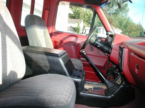 1990 Ford F-250 - The interior of a red Ford F-250 truck shows a custom black center console with cup holders, a floor-mounted shifter, and gray fabric seats…