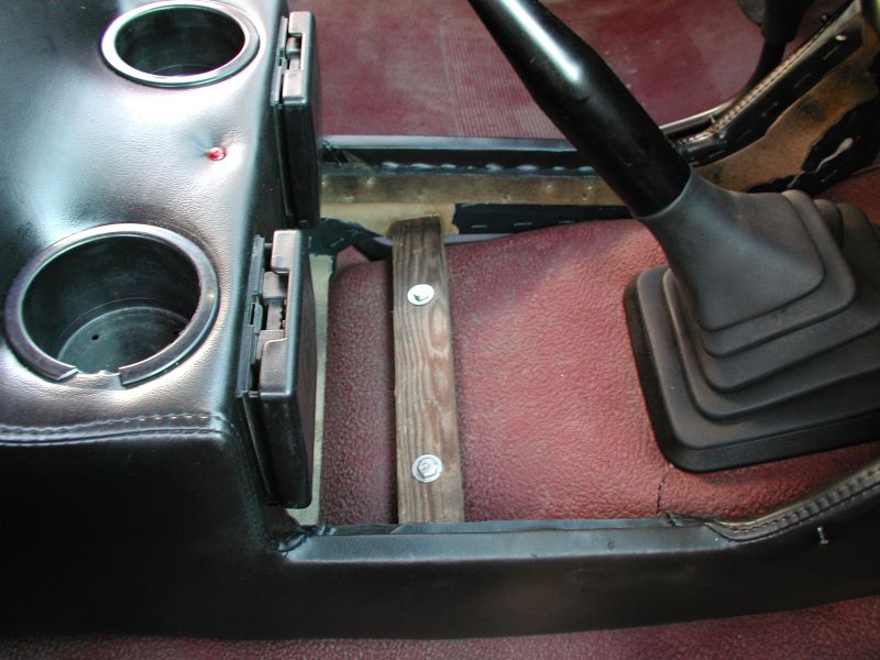 Interior of a vehicle showing a center console with cup holders and a gear shifter, with a wooden block support.