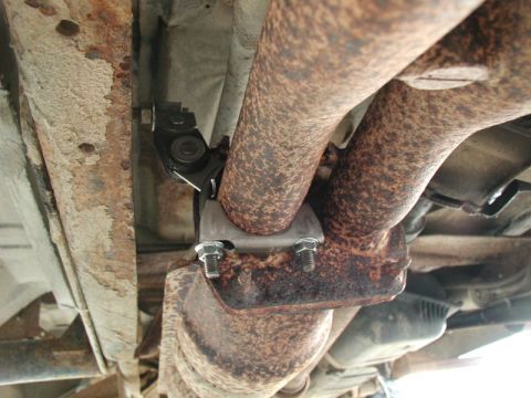 1990 Ford F-250 - A close-up, low-angle view of the rusted exhaust system of a vehicle, showing a newly installed catalytic converter clamp with bolts and nu…