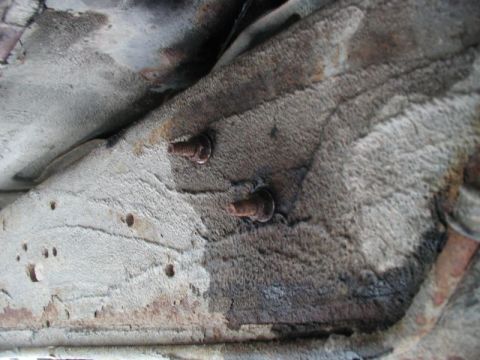 1990 Ford F-250 - Two rusty bolts are visible on the underside of a vehicle frame, which appears to be coated in a light-colored undercoating that is peeling…